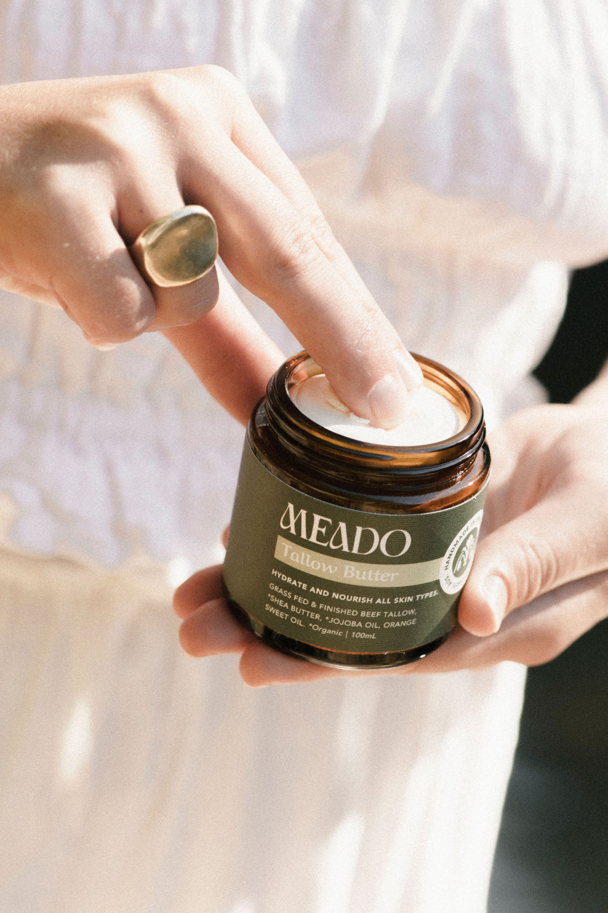 Close-up of fingers dipping into creamy whipped tallow body butter, showcasing rich texture of natural beef tallow skincare for nourishing dry, sensitive skin.