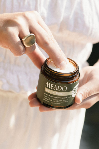 Close-up of fingers dipping into creamy whipped tallow body butter, showcasing rich texture of natural beef tallow skincare for nourishing dry, sensitive skin.