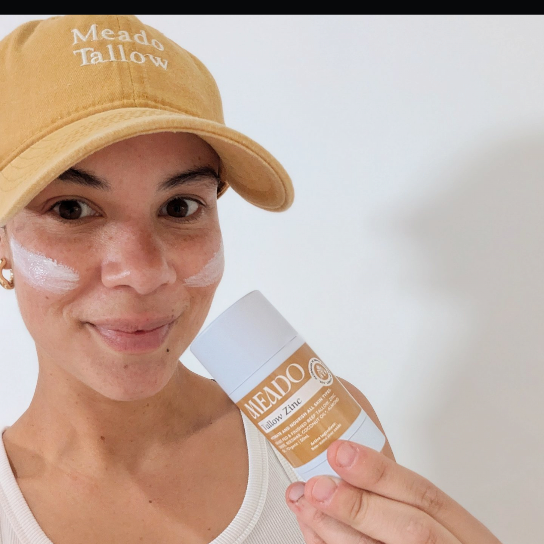 Person wearing a beige cap with text, holding a product labeled 'tallow zinc' against a plain background.